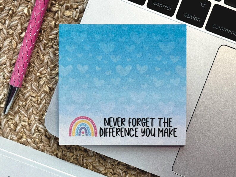 May include: A square sticky note with a blue gradient background featuring a pattern of light blue hearts. The bottom left corner displays a colorful rainbow icon, and the text reads, "NEVER FORGET THE DIFFERENCE YOU MAKE" in black.