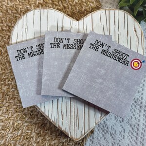 May include: Three gray sticky notes with the text "Don't Shoot The Messenger" on each. The third note has a red and yellow target with an arrow in the center.