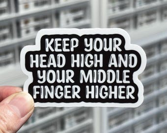 May include: A die-cut sticker with a black background and a white border. The text in white, bold, sans-serif font reads: KEEP YOUR HEAD HIGH AND YOUR MIDDLE FINGER HIGHER. The sticker has a matte finish and a distinct, irregular shape following the text.