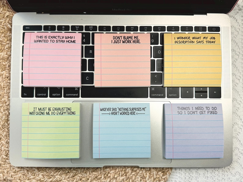 May include: A laptop keyboard with six colourful sticky notes. The notes have humorous phrases like "This is exactly why I wanted to stay home" and "Don't blame me I just work here."