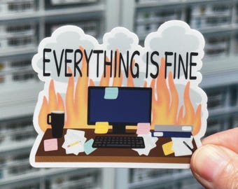 May include: A die-cut sticker featuring a computer desk scene with a monitor, keyboard, and scattered papers. The background shows orange flames and grey smoke. The text "EVERYTHING IS FINE" is printed in black letters across the top of the sticker.