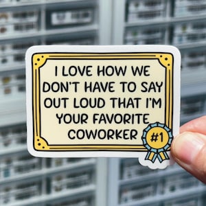 May include: A yellow and white sticker with a gold frame and a blue ribbon. The sticker says "I love how we don't have to say out loud that I'm your favorite coworker #1".