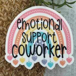Puede incluir: Una pegatina troquelada con un arco&iacute;ris de colores pastel y el texto negro "emotional SUPPORT COWORKER" impreso en el centro. El dise&ntilde;o del arco&iacute;ris incluye peque&ntilde;as formas de coraz&oacute;n colgantes en rosa, amarillo, azul y morado en la base.