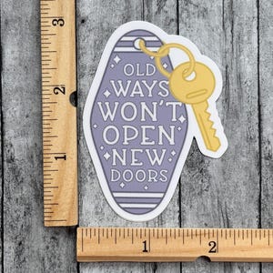 Pu&ograve; includere: Un adesivo a forma di portachiavi da motel color viola chiaro con l'illustrazione di una chiave gialla e il testo OLD WAYS WON'T OPEN NEW DOORS. Un righello in legno mostra che l'adesivo misura circa 7,6 cm in altezza e 3,8 cm in larghezza.