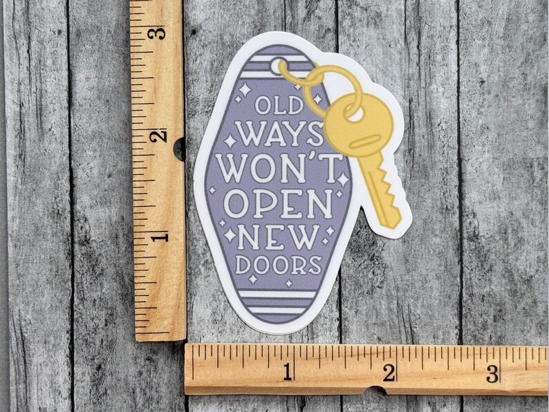 Pu&ograve; includere: Un adesivo a forma di portachiavi da motel color viola chiaro con l'illustrazione di una chiave gialla e il testo OLD WAYS WON'T OPEN NEW DOORS. Un righello in legno mostra che l'adesivo misura circa 7,6 cm in altezza e 3,8 cm in larghezza.