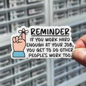 May include: White sticker with a black outline and a cartoon finger with a reminder note that reads "REMINDER IF YOU WORK HARD ENOUGH AT YOUR JOB, YOU GET TO DO OTHER PEOPLE'S WORK TOO."