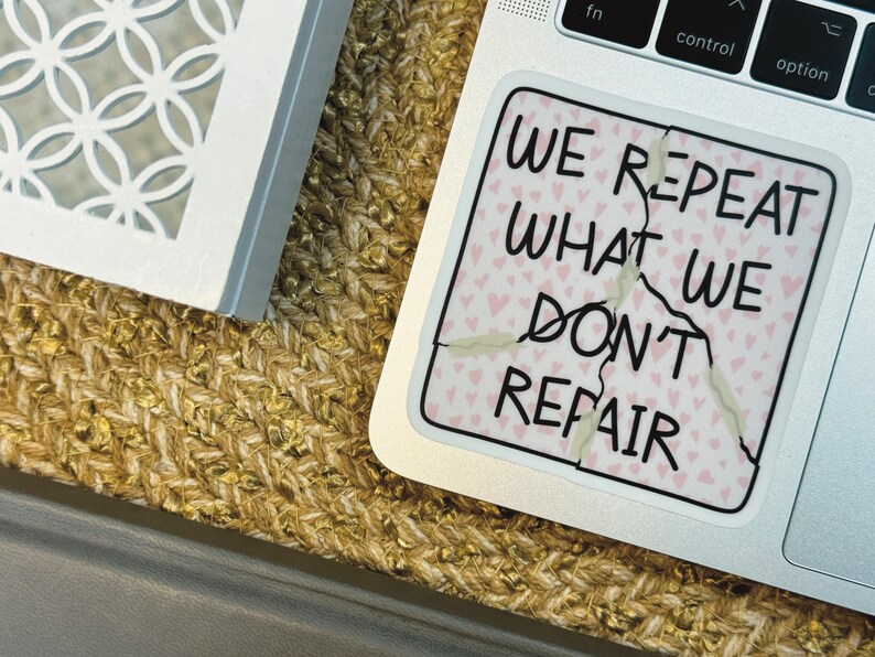 May include: A white laptop with a sticker that says "We repeat what we don't repair". The sticker is cracked and has a pink background with small pink hearts.