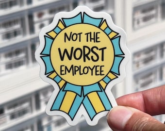 May include: A die-cut sticker shaped like a circular award ribbon with a yellow center and light blue and yellow pleated edges. The text NOT THE WORST EMPLOYEE is printed in black, bold, sans-serif capital letters across the center of the ribbon.