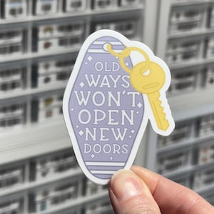 May include: A light purple motel-style keychain sticker with white horizontal stripes and the text "OLD WAYS WON'T OPEN NEW DOORS" in white lettering. A yellow key is attached to the top of the keychain, which is decorated with small white stars.