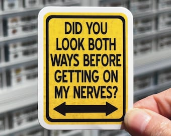 May include: A rectangular yellow sticker with a black border and black text that reads: DID YOU LOOK BOTH WAYS BEFORE GETTING ON MY NERVES? A black horizontal arrow pointing in both directions is positioned at the bottom of the sticker.