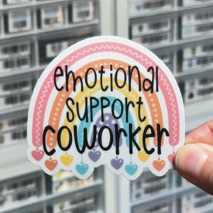 May include: A rainbow-colored sticker with the text "emotional support coworker" in black lettering. The sticker has a rainbow design with hearts at the bottom.