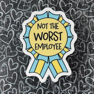 May include: A sticker with the text "NOT THE WORST EMPLOYEE" in black, yellow, and blue. The sticker is shaped like a ribbon and is set against a black background with white heart doodles.