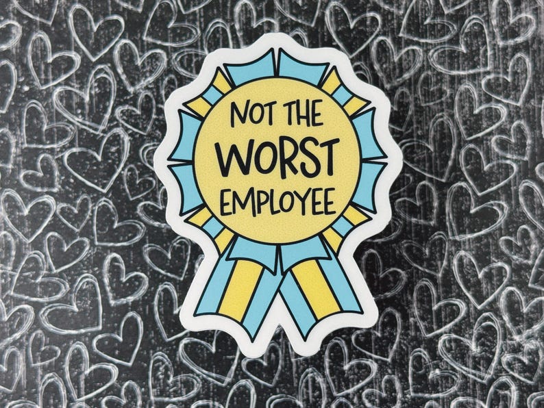 May include: A sticker with the text "NOT THE WORST EMPLOYEE" in black, yellow, and blue. The sticker is shaped like a ribbon and is set against a black background with white heart doodles.