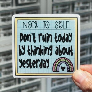 May include: A square sticker with a light blue background and a yellow border. The sticker has the text "NOTE TO SELF Don't ruin today by thinking about Yesterday" in black. A rainbow and heart graphic is at the bottom.