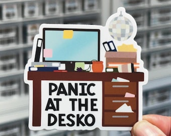 May include: A die-cut sticker featuring a brown desk with a computer monitor, a disco ball, and office supplies. The text "PANIC AT THE DESKO" is printed in bold black letters on the front of the desk, which includes three drawers and various papers.