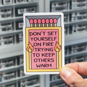 May include: A pink and yellow sticker with a matchbox design. The text on the sticker reads "Don't set yourself on fire trying to keep others warm."