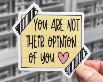 May include: A yellow rectangular sticker resembling a lined notepad page with black text that reads, "YOU ARE NOT THEIR OPINION OF YOU" followed by a pink heart. The sticker is decorated with two pieces of black and white striped tape at the corners.