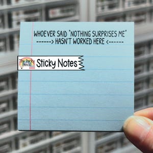 May include: A light blue sticky note with horizontal blue lines and a red vertical line. The text reads: "WHOEVER SAID 'NOTHING SURPRISES ME' ------> HASN'T WORKED HERE <-----". The sticky note has the words "Sticky Notes" and "The Perky Pencil" on it.