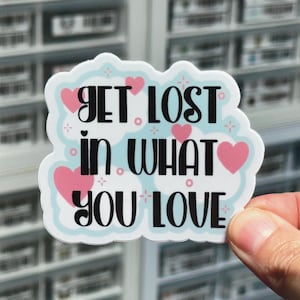 May include: A white sticker with a blue background and pink hearts. The sticker says "Get lost in what you love."