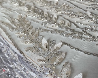 Peut inclure: Tissu blanc perlé avec un motif floral délicat. Le tissu est fait de paillettes et de perles, et il a une texture douce et fluide.