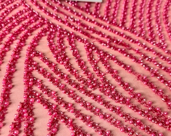 May include: Pink beaded fabric with a wavy pattern. The fabric is made of a sheer mesh with small pink beads sewn onto it.