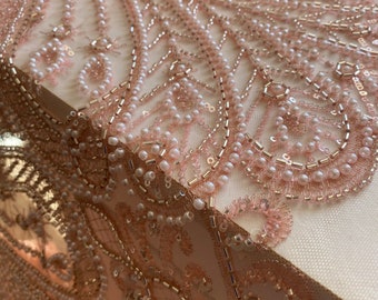Peut inclure: Gros plan sur un tissu rose délicat avec des perles et des paillettes complexes. Le tissu présente un motif de lignes et de formes tourbillonnantes, créant un aspect luxueux et élégant.
