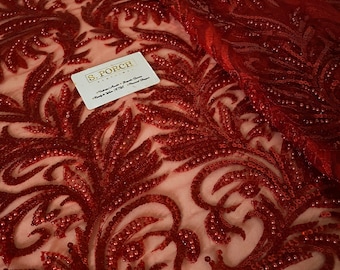 Peut inclure: Tissu de dentelle rouge perlé avec un motif floral. Le tissu est transparent et a une texture délicate. Les perles sont petites et uniformément espacées. Le tissu est parfait pour faire des robes, des jupes et d'autres vêtements.