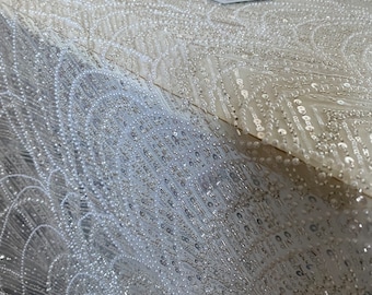 May include: White beaded fabric with a geometric pattern. The beads are small and create a shimmering effect.