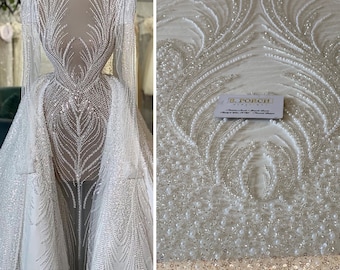 Peut inclure: Tissu de dentelle blanche perlée avec un motif floral délicat. Le tissu est orné de petites perles et de paillettes. Le tissu est parfait pour créer un look luxueux et élégant.