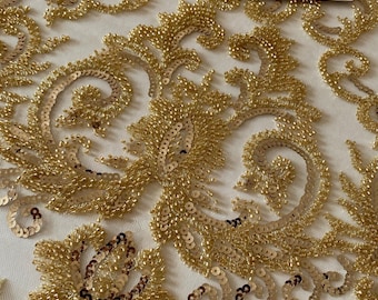 Peut inclure: Gros plan sur un tissu doré orné de perles et de sequins, avec un motif floral élaboré. Le tissu de base est crème clair, avec des embellissements dorés. Le tissu a un aspect luxueux, idéal pour les tenues de soirée ou les projets décoratifs.