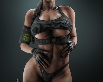May include: A dark gray ribbed athletic crop top with a cutout, matching high-cut bottoms, fingerless gloves, and an arm band featuring a green skull graphic. The outfit includes a holster on the thigh and aviator sunglasses. The text K I S X is visible.