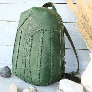 Op de afbeelding: Een groene leren rugzak met decoratieve stiksels en een ritssluiting. De rugzak heeft een uniek ontwerp met een gegolfde rand en een geometrisch patroon.