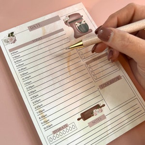 May include: A beige and brown planner with a floral design. The planner has a section for "Today" and "Tomorrow" with a list of times from 6:00 am to 10:00 pm. The planner also has a section for "To Do" and "Notes". There is a graphic of a kitchen mixer and a rolling pin on the planner.