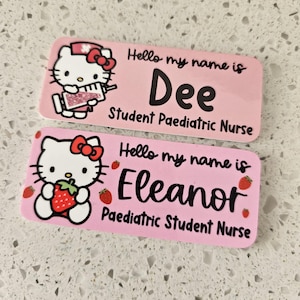 May include: Two rectangular pink name badges featuring Hello Kitty graphics. The top badge reads Hello my name is Dee Student Paediatric Nurse with a syringe graphic. The bottom badge reads Hello my name is Eleanor Paediatric Student Nurse with strawberries.