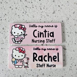 May include: Two rectangular name badges with a light pink background. The top badge features Hello Kitty holding a syringe and the text Hello my name is Cintia Nursing Staff. The bottom badge shows Hello Kitty with a baby and the text Hello my name is Rachel Staff Nurse.