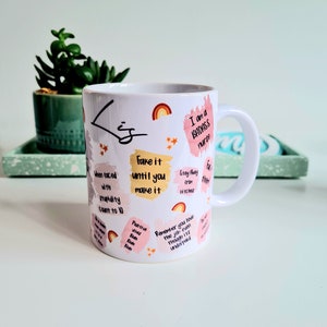 Puede incluir: Taza de cer&aacute;mica blanca con un dise&ntilde;o rosa y amarillo. La taza tiene un asa y presenta citas inspiradoras y el texto "I am a BADASS nurse".
