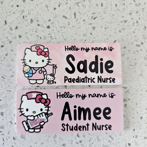 May include: Two rectangular pink name badges featuring Hello Kitty illustrations. The top badge reads Hello my name is Sadie Paediatric Nurse with a nurse Hello Kitty holding a baby. The bottom badge reads Hello my name is Aimee Student Nurse with a nurse Hello Kitty holding a syringe.