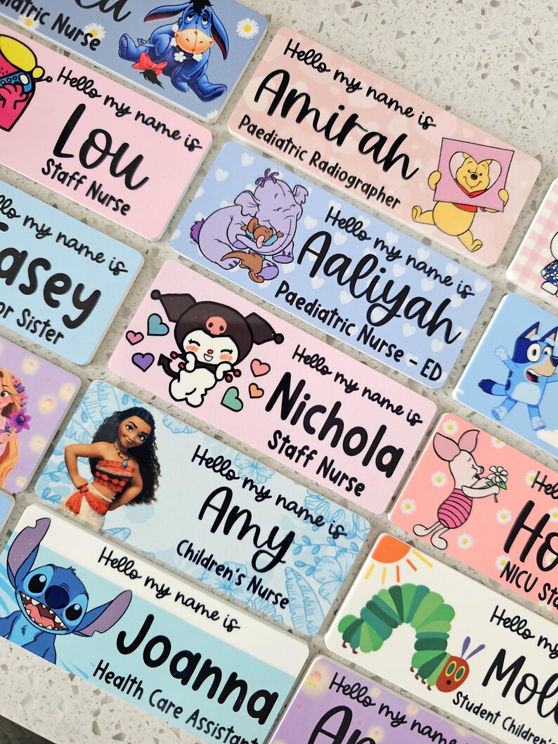 May include: A collection of rectangular name badges featuring the text Hello my name is followed by various names and job titles. Each badge displays colorful cartoon characters including Winnie the Pooh, Stitch, Moana, and Piglet on pastel backgrounds.