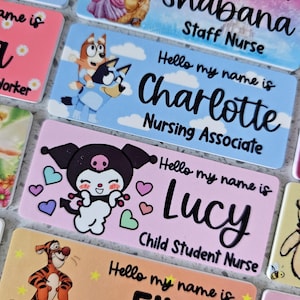 May include: A collection of rectangular name badges featuring various cartoon characters and printed text. Each badge displays the phrase Hello my name is followed by a name and job title, including Shabana Staff Nurse, Charlotte Nursing Associate, and Lucy Child Student Nurse.