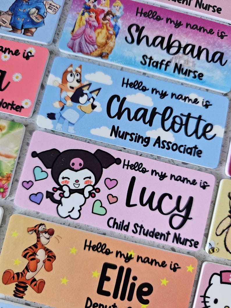 May include: A collection of rectangular name badges featuring various cartoon characters and printed text. Each badge displays the phrase Hello my name is followed by a name and job title, including Shabana Staff Nurse, Charlotte Nursing Associate, and Lucy Child Student Nurse.