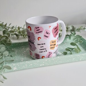 Puede incluir: Taza de caf&eacute; de cer&aacute;mica blanca con un dise&ntilde;o rosa y blanco. La taza tiene varias frases impresas en ella, incluyendo "No recurras a la violencia", "Fingelo hasta que lo logres" y "Soy una enfermera ruda".