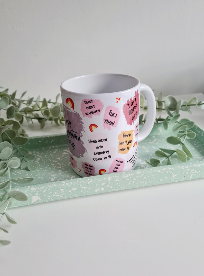 Puede incluir: Taza de caf&eacute; de cer&aacute;mica blanca con un dise&ntilde;o rosa y blanco. La taza tiene varias frases impresas en ella, incluyendo "No recurras a la violencia", "Fingelo hasta que lo logres" y "Soy una enfermera ruda".