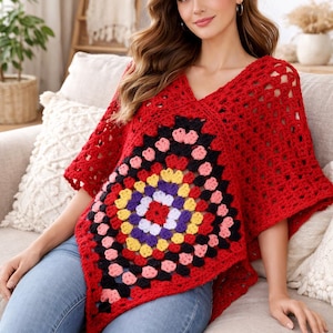 Peut inclure: Un poncho rouge en crochet avec un col en V et des manches courtes. Le poncho présente un grand motif de granny square coloré au centre, avec des accents noirs, roses, jaunes, violets et blancs. Le modèle porte un jean bleu.