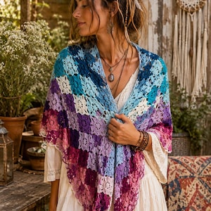 Peut inclure: Un châle en crochet coloré dans les tons de bleu, violet et rose. Le châle est drapé sur une robe blanche. Le motif au crochet présente un motif floral. Le châle est de forme triangulaire.