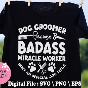 May include: Black t-shirt with white text that reads "Dog Groomer Because Badass Miracle Worker Isn't An Official Job Title". The text is surrounded by images of a comb, scissors, and paw prints.