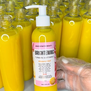 Puede incluir: Una botella de gel de ducha iluminador de plástico amarillo con una tapa de bomba blanca. La etiqueta de la botella dice "Awakened by Nature's Beauty Brightening Turmeric & Vitamin C Shower Gel".