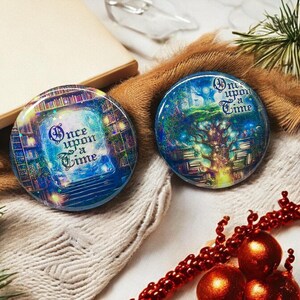 May include: Two round, blue and gold pinback buttons with a whimsical fairytale theme. The buttons feature the text "Once Upon a Time" and illustrations of a book-filled forest and a magical doorway.