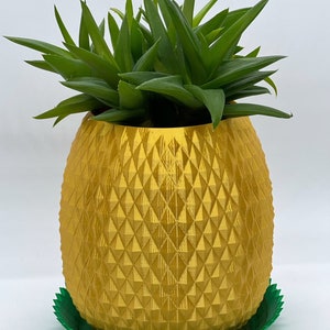 May include: A bright yellow, pineapple-shaped planter with a textured, diamond-patterned surface. The planter sits inside a vibrant green, scalloped-edge saucer. A green succulent plant with pointed leaves is planted inside the yellow container.