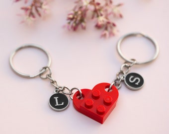 May include: A red heart-shaped LEGO keychain with the letters "L" and "S" on silver charms attached to two silver key rings.