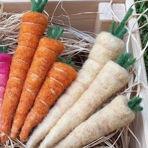 May include: A close-up of a wooden crate filled with felt carrots and parsnips. The carrots are orange and the parsnips are a pale yellow. The vegetables are arranged in a visually appealing way.
